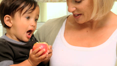 baby in mothers arms tasting a red apple