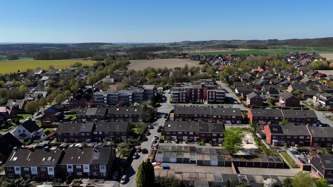 Historic two-story townhouses and garages in small american town. Aerial lateral wide shot. Farm fields and hills with blue sky in springtime. Cars on street during sunny day. Low income apartments.