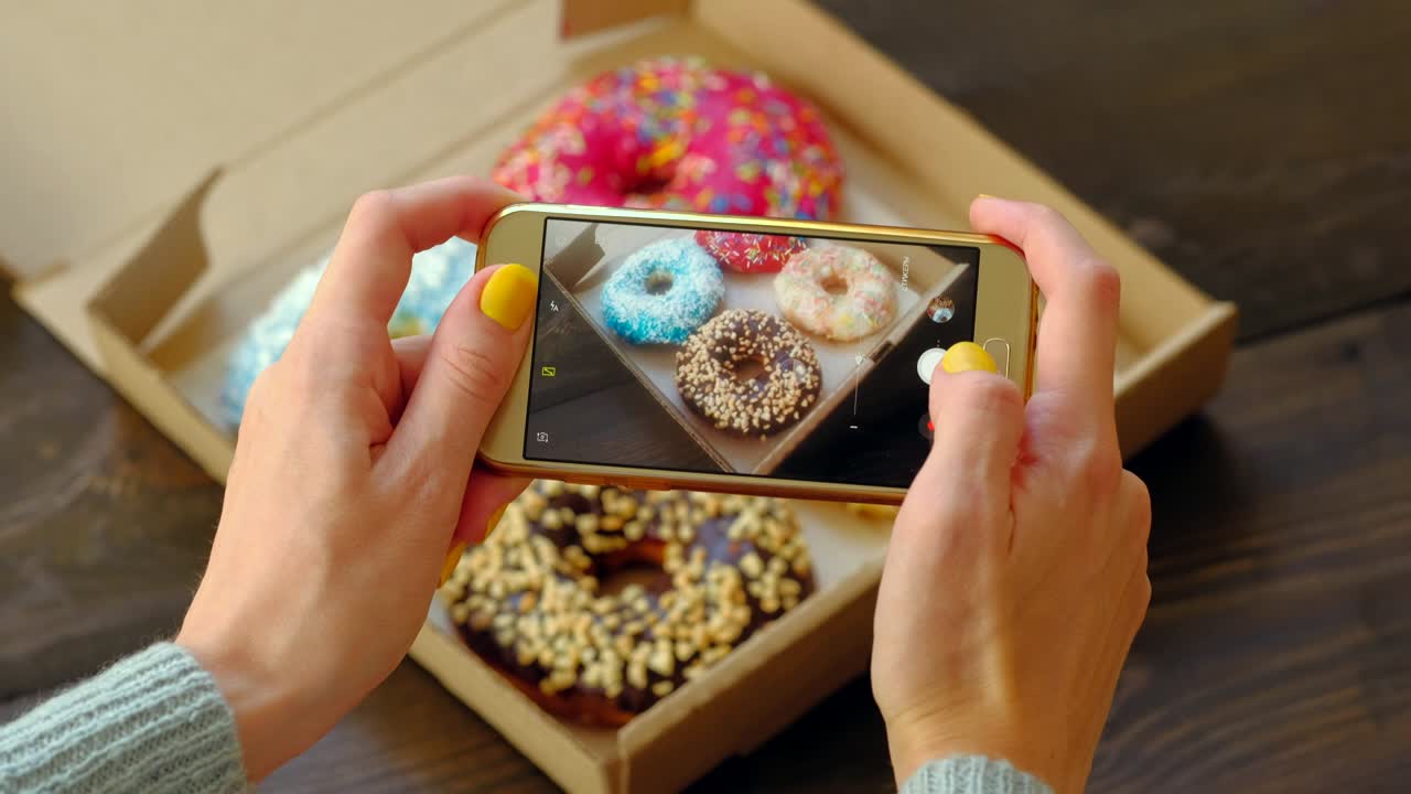 las manos de la mujer toman fotos con el teléfono inteligente de deliciosas rosquillas en la caja