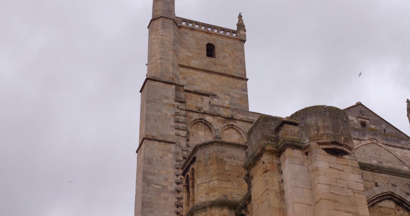 Vista dal basso del campanile della Cattedrale di Narbonne contro un cielo nuvoloso e drammatico.