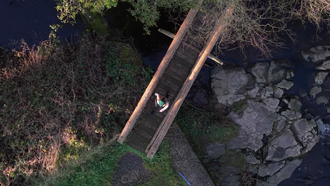 Donna attraversa un ponte sulle cascate di Cathole, atmosfera serena nella foresta, Laois, Irlanda.
