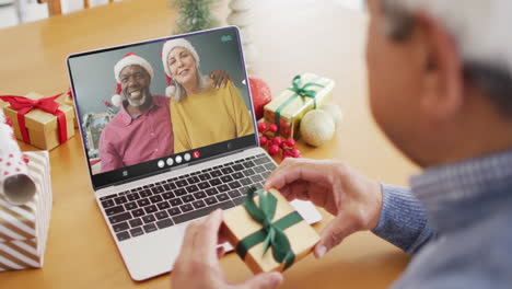 biracial man with gift having laptop video call with happy diverse couple