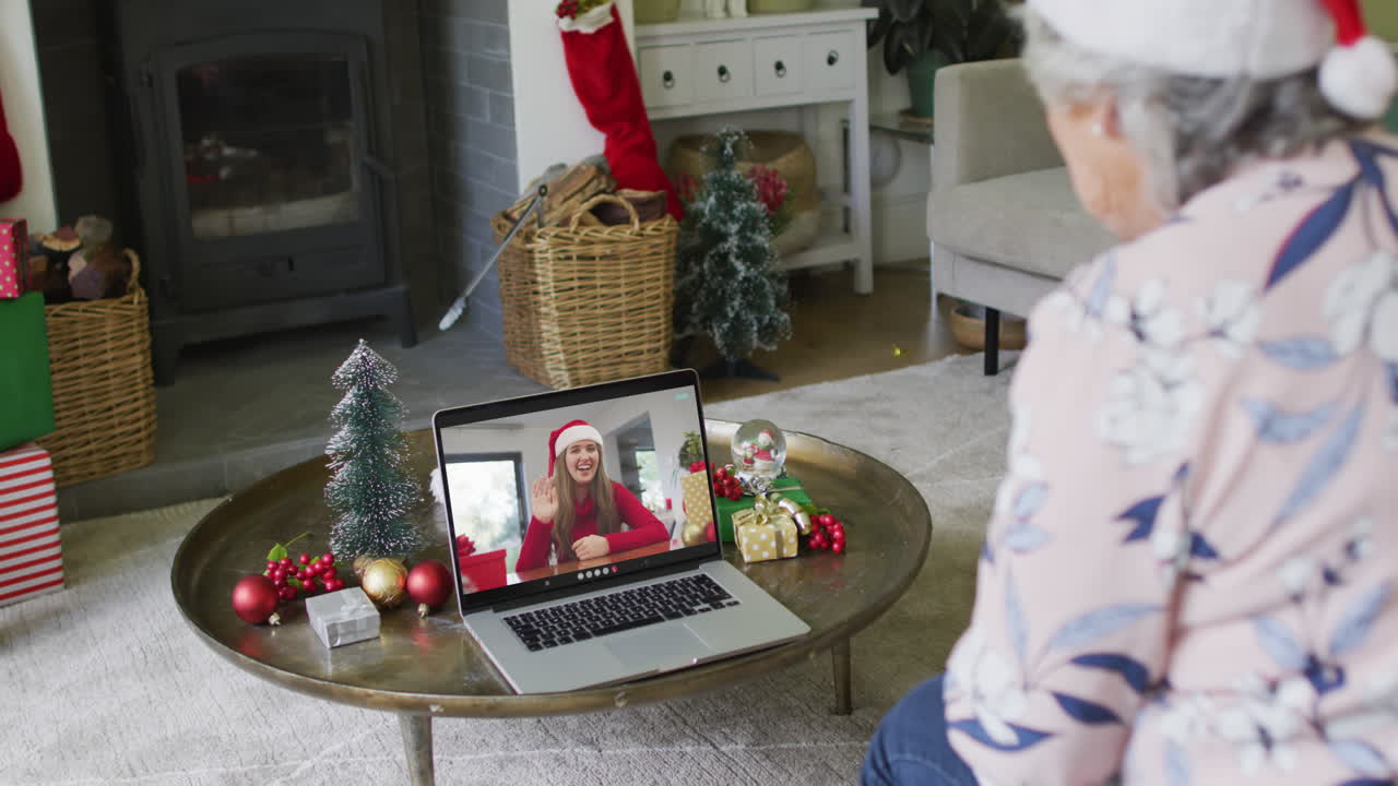 mujer mayor caucásica usando una computadora portátil para una videollamada de navidad con una mujer sonriente en la pantalla