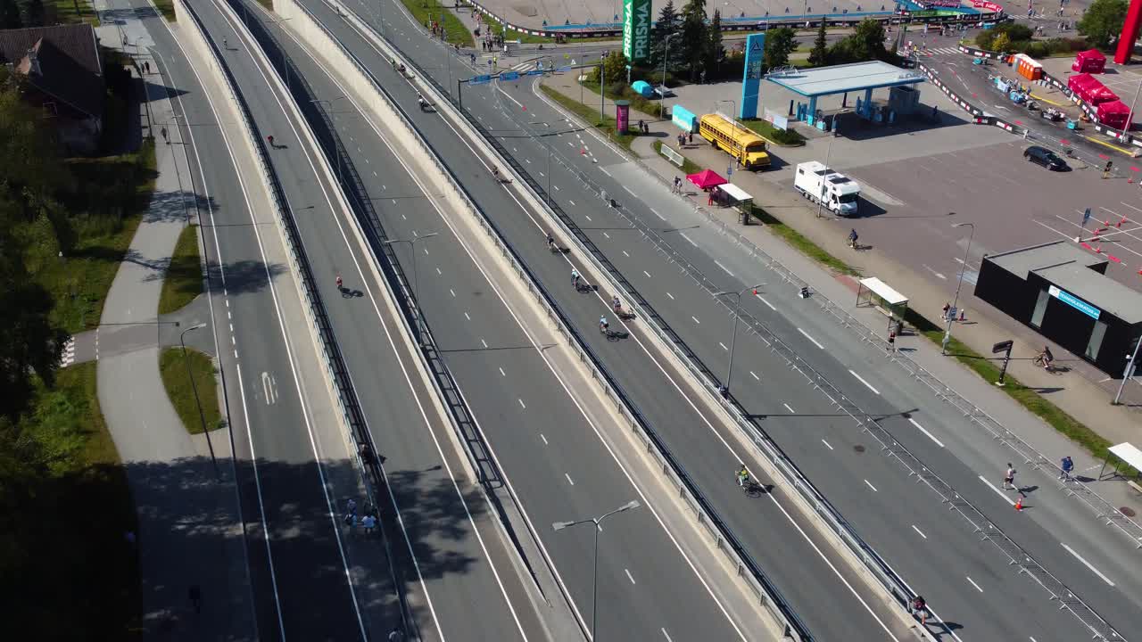 Drone footage capturing the tallinn triathlon, showcasing cyclists on an elevated road, green landscapes, and urban surroundings on a clear day