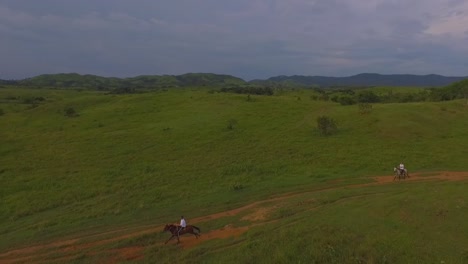 Two-riders-galop-their-horses-in-a-red-dirt-road-in-a-venezuelan-plain,-slow-motion