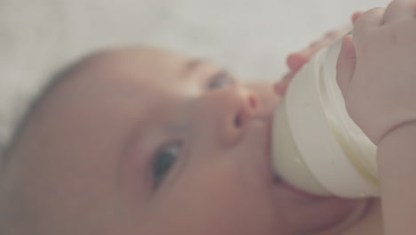 Closeup-milk-bottle-baby-feeding-himself-holding-independently,-makes-eye-contact