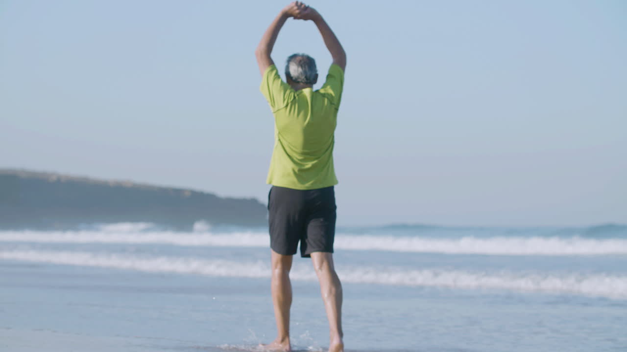 성숙한 남자가 바다 연안을 따라 고 팔을 들어 올립니다.