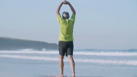 mature man walking along ocean coast and raising arms up