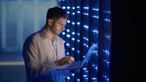 it technician in data center digital server room controlling work of rack server cabinets with a tablet. professional server engineer at work.