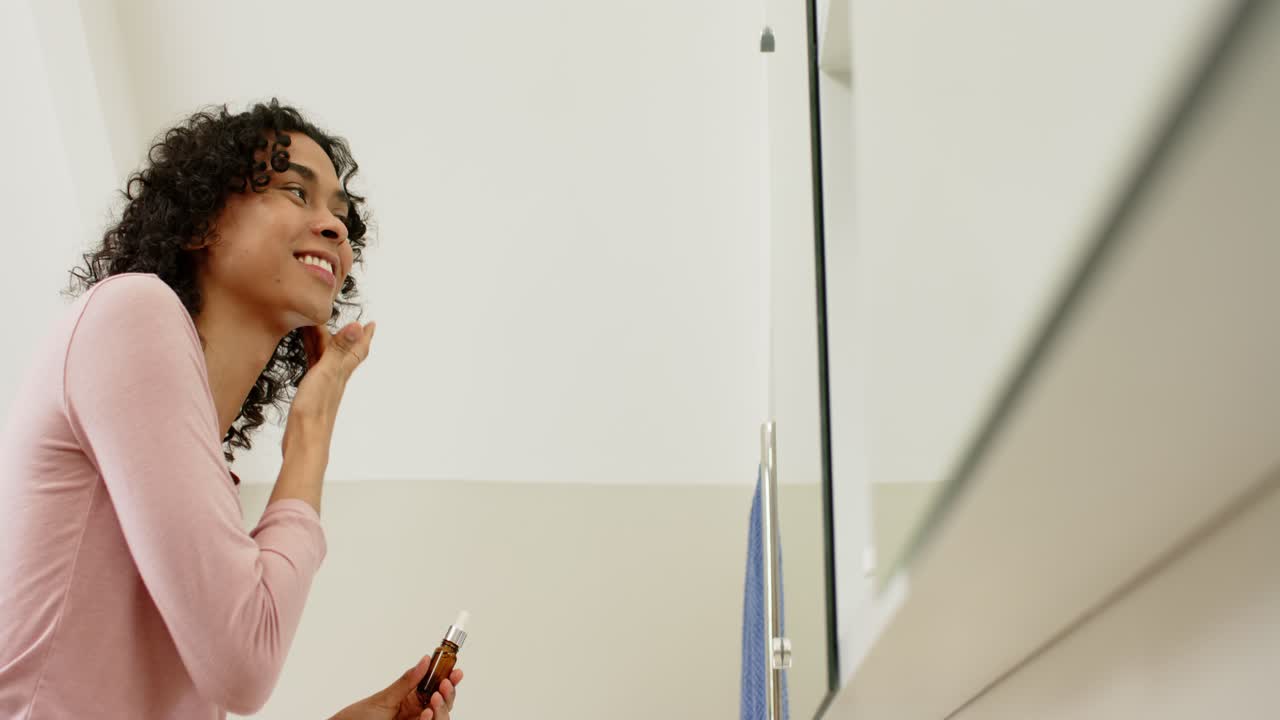 Persona non binaria che rimuove il tappo del contagocce, spreme gocce di siero e lo applica allo specchio del bagno.