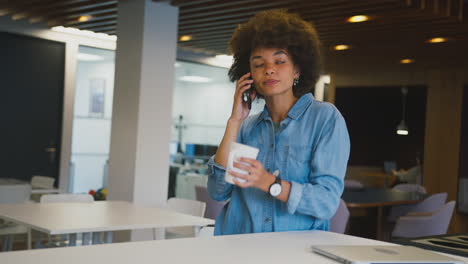 mujer de negocios de pie en una oficina moderna de plan abierto hablando por teléfono móvil
