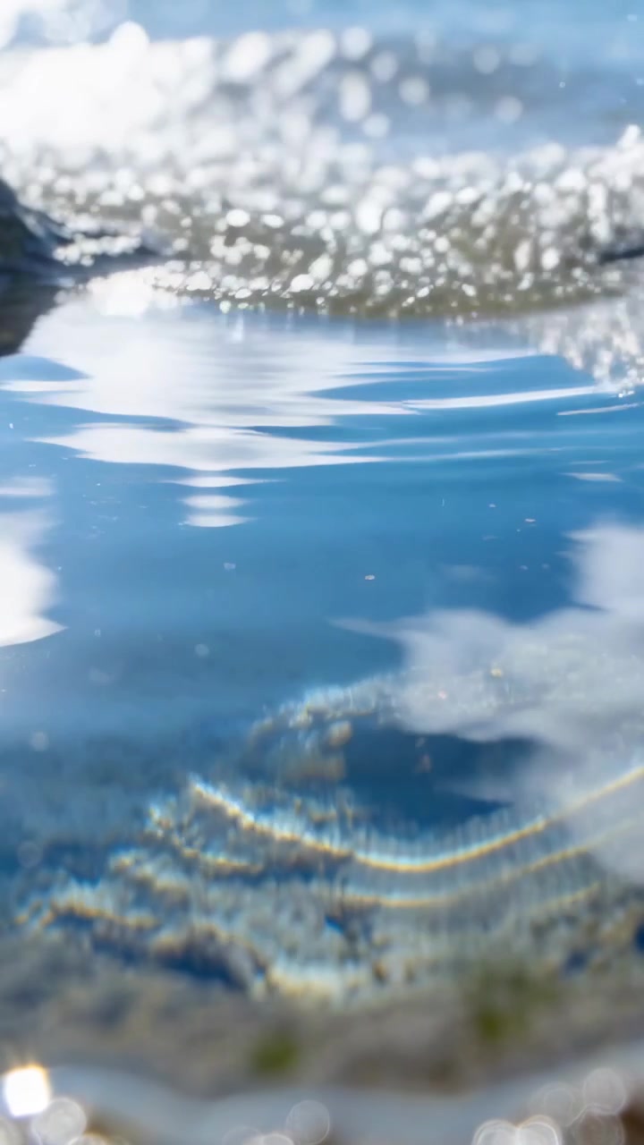 Superfície de piscina natural mudando de calma para agitada, ondas propagando ondulações obscurecendo rochas.