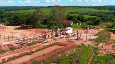 sitio de extracción de arena con equipos de dragado industrial rodeado de vegetación y campos abiertos.