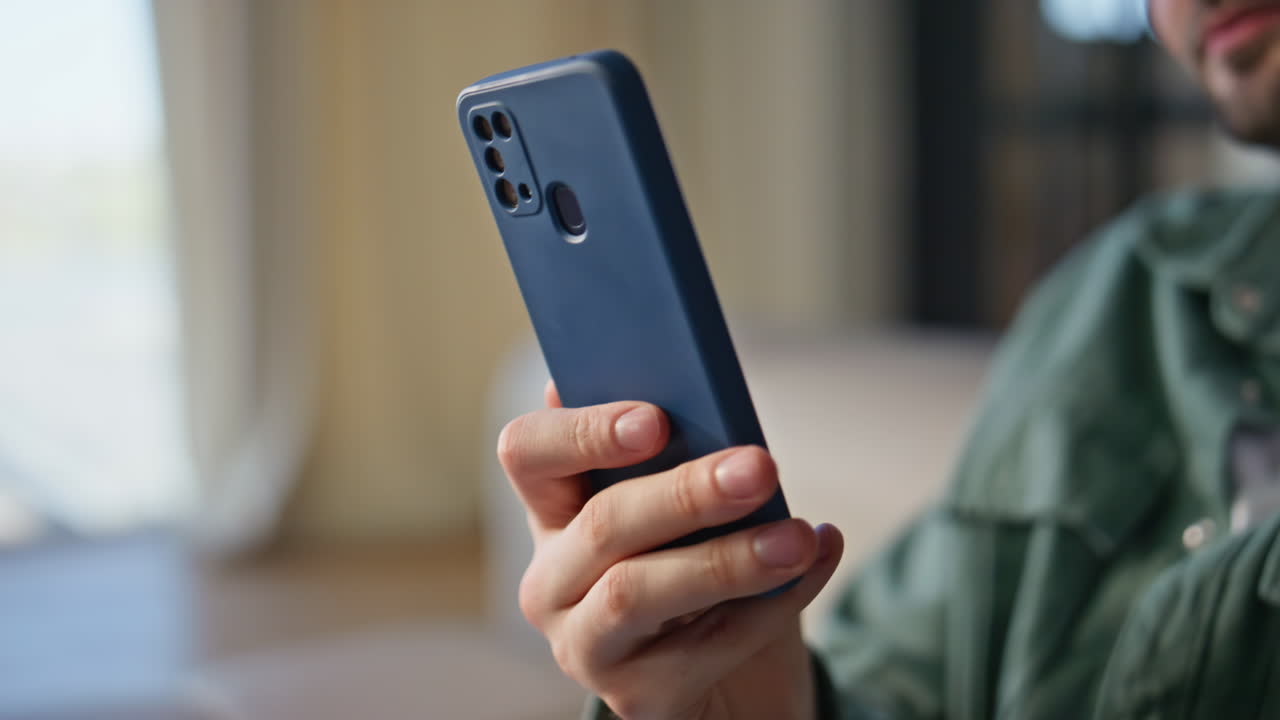 User hand holding smartphone at home closeup. Relaxed man watching cellphone