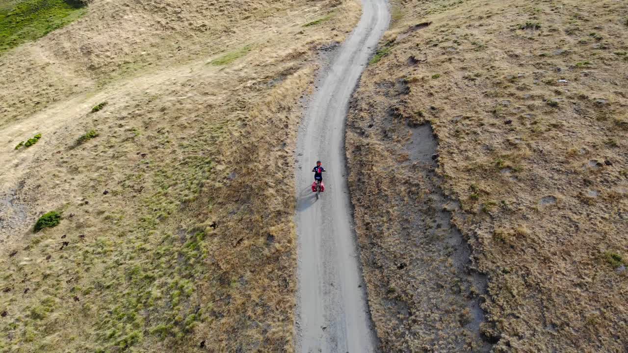 Aerial: mountain biker going downhill in a high mountain deserted area in summer time
