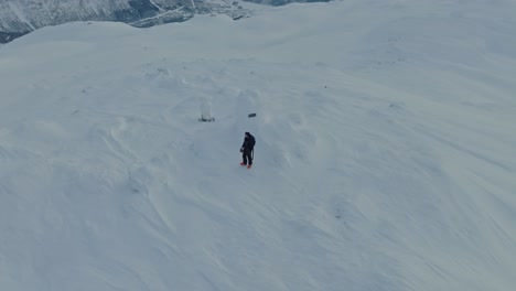 Skier-alone-on-top-of-summit-Finnbunuten-in-snow-covered-landscape-Myrkdalen-Norway---Aerial-roating-above-man-while-changing-altitude-and-background