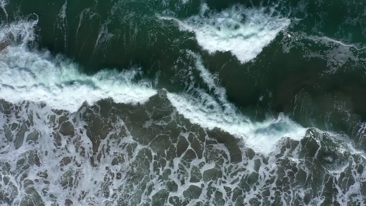 Top down drone shot of West Coast waves crashing on a rocky shore