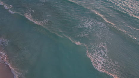 aerial top down shot of rolling waves in a crystal clear blue ocean with white sand beach in cancun, mexico