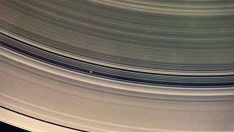 close shot of a moon orbiting within the rings of the gas giant saturn