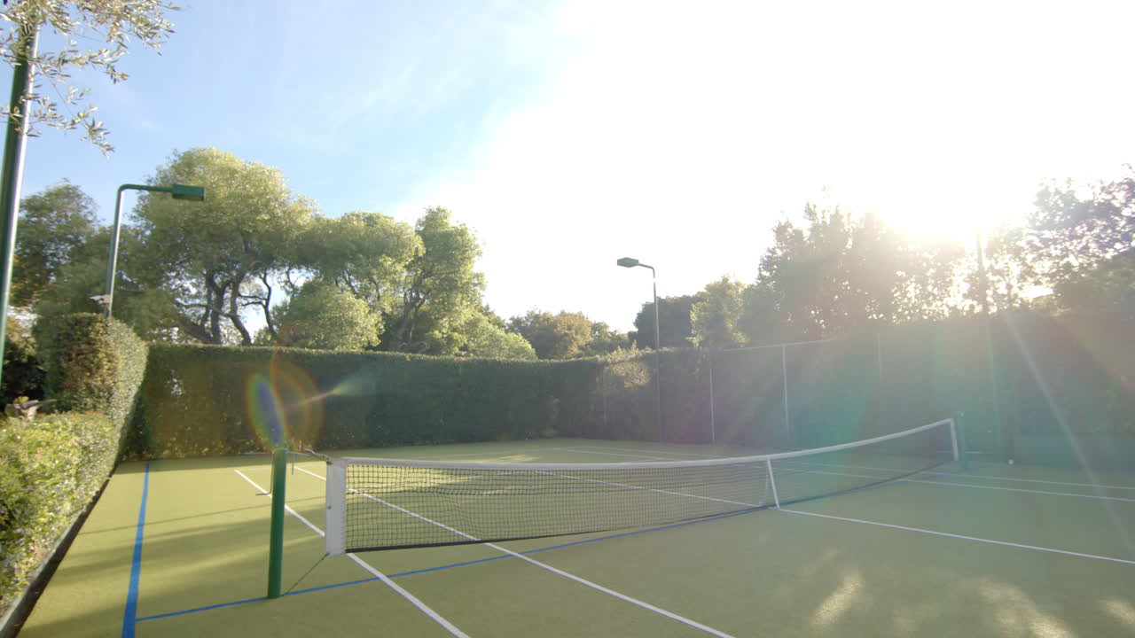 Luce solare intensa su un campo da tennis vuoto circondato da alberi