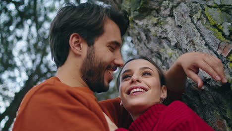 romantic man hugging woman leaning tree vertically closeup. young pair laughing