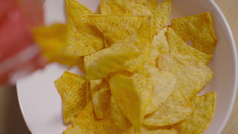 fotografía aérea de una persona en casa vertiendo tortilla o papas fritas de maíz de un paquete en un cuenco en la mesa
