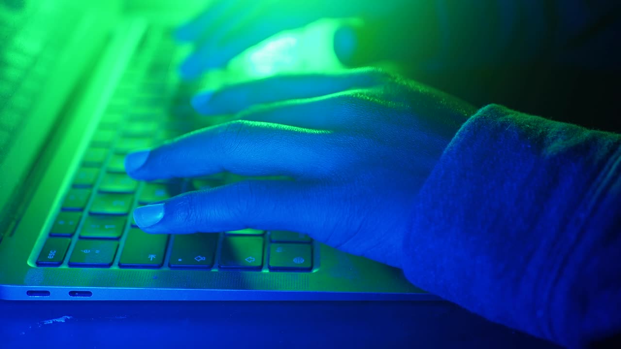 Person typing on a laptop at night with colored light