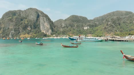 idyllic emerald sea water tonsai bay with group of docked long-tail boats in ko phi phi don island in thailand - aerial low fly-over slide shot