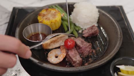 removing shrimp and vegetables from skewer to sizzling plate with beef steak and rice