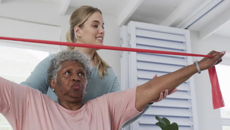 caucasian nurse with senior woman exercising with rubber band, copy space, slow motion