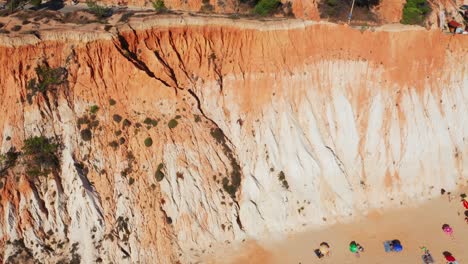 aerial shot of praia da falesia red cliff face and beach with waves crashing along the shore, portugal