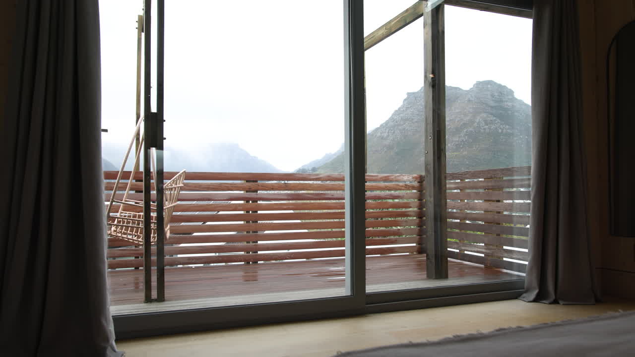 Cozy bedroom with mountain view through open sliding glass doors on rainy day, copy space