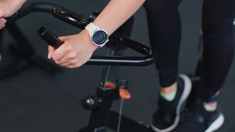 Close-up-athletic-woman-spin-exercising-workout-on-stationary-cycle-machine-bike,-indoors