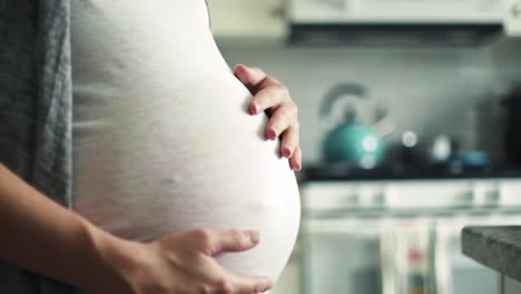 pregnant woman gently cradles her baby bump in a cozy kitchen setting, showcasing the beauty of motherhood and anticipation of new life