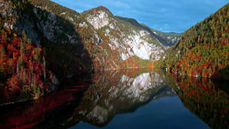 white and green forested mountain reflects in water of lake toplitz, aerial dolly
