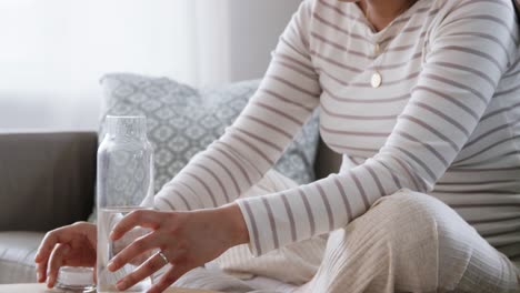 Mujer-Embarazada-Con-Agua-En-Botella-De-Vidrio-En-Casa.-Concepto-De-Embarazo,-Descanso,-Personas-Y-Expectativas.-Feliz-Sonriente-Mujer-Embarazada-Asiática-Sentada-En-Un-Sofá-En-Casa-Y-Bebiendo-Agua-De-Una-Botella-De-Vidrio-Reutilizable.