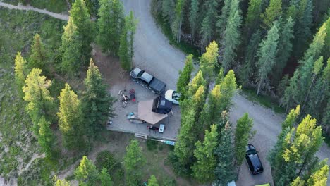 birds eye view of a campsite with a rooftop tent setup and a couple vehicles surrounded by large pine trees