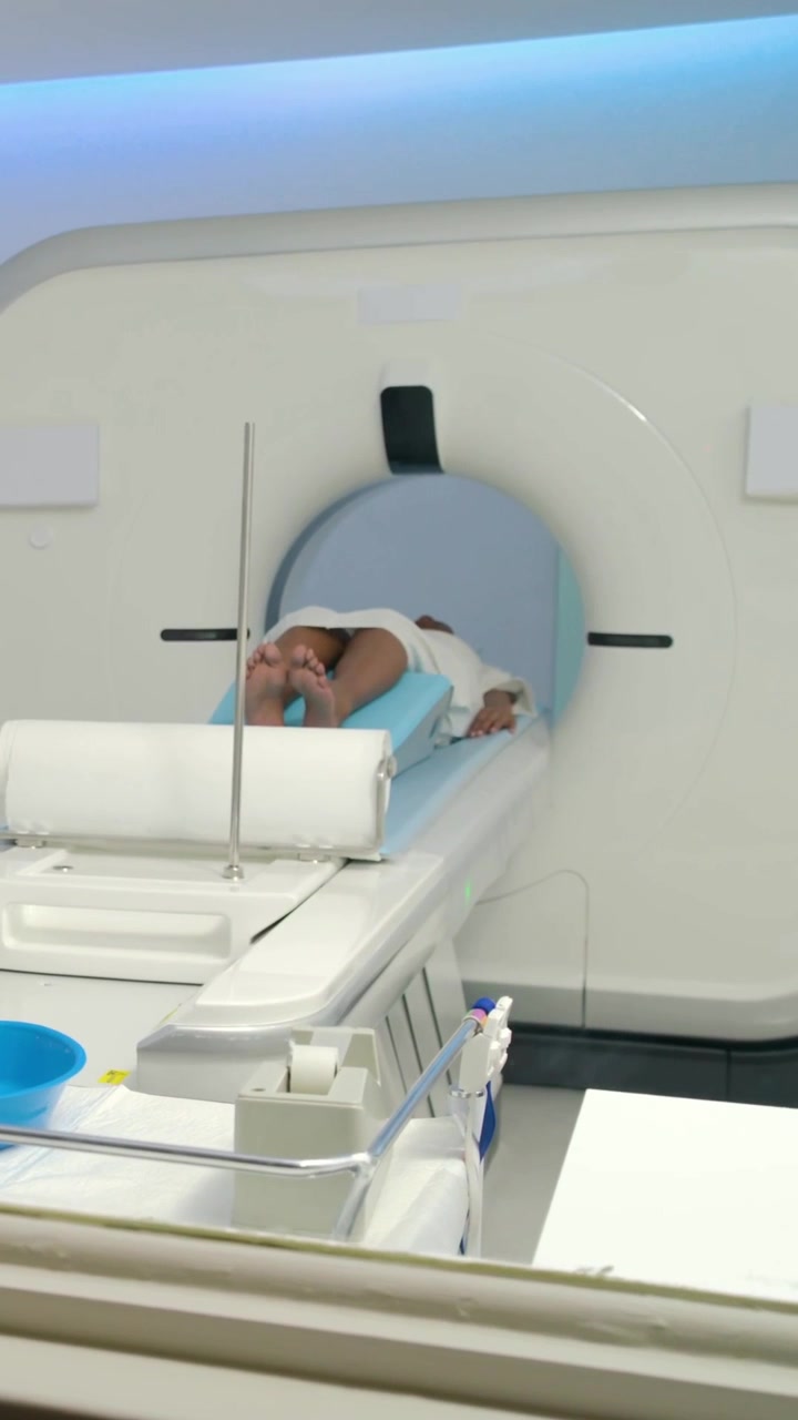 Video verticale: Il motore del tavolo si avvia, paziente in camice che scivola a testa in giù nello scanner per una TAC.