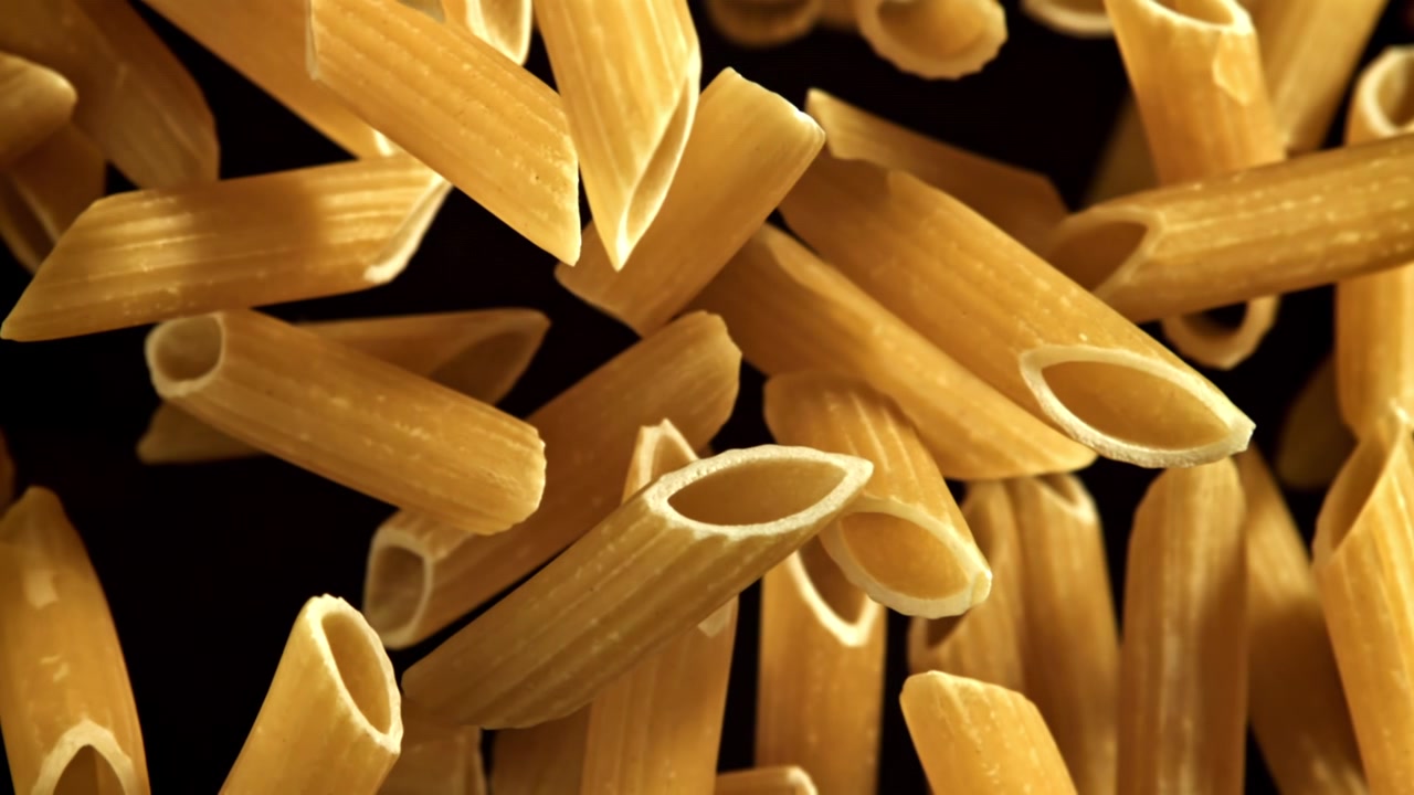 Pasta penne cruda che cade al rallentatore su sfondo nero