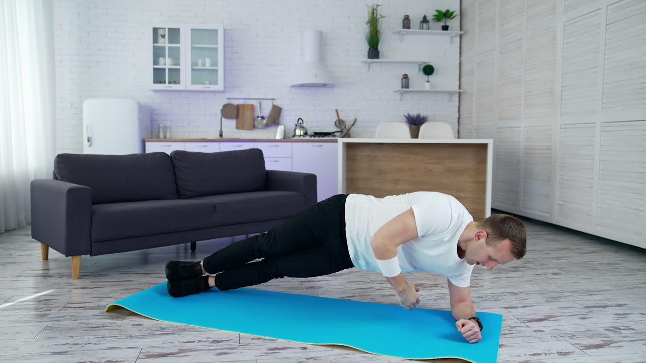 Young man is training at home. Man doing exercise on a mat on kitchen background. Guy working hard to maintain body shape during isolation.