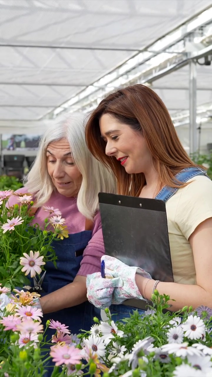 Due donne che ispezionano fiori in vaso in una serra.