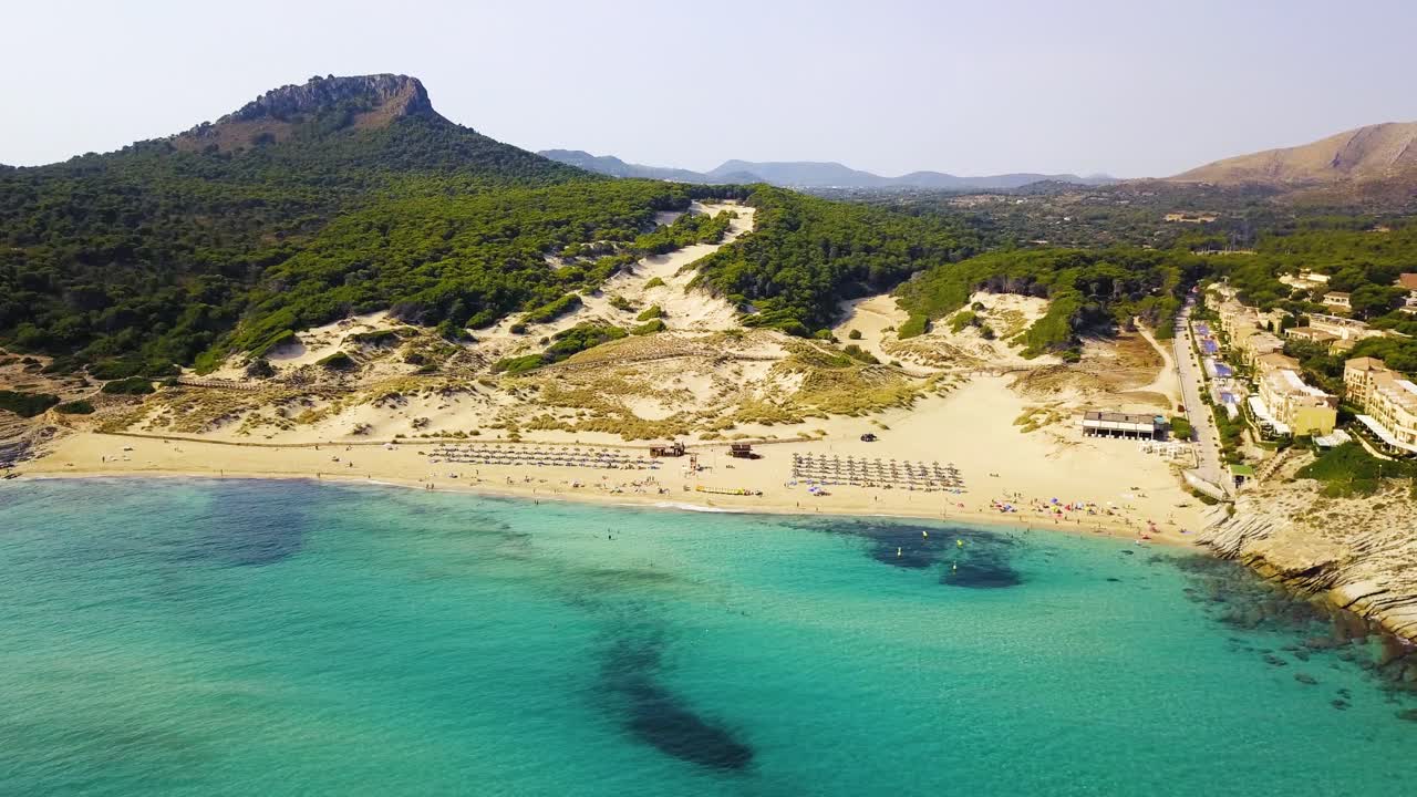 Dron realizando un paneo de izquierda a derecha de la costa de Cala Mesquida, mostrando toda la extensión de la costa y bosques montañosos a lo lejos, en la isla de Mallorca, España.