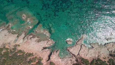 crystalline blue sea with waves crashing against the rocks of the mediterranean coast in sardinia, italy - aerial, top down