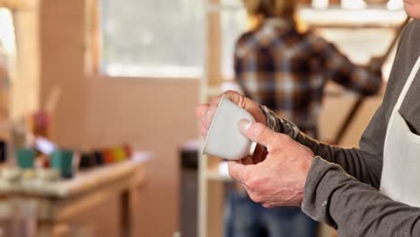 Mid-section-of-male-potter-checking-a-cup