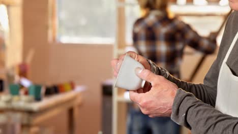 mid-section of male potter checking a cup