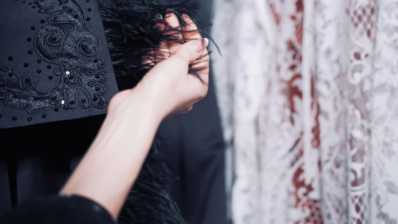 Woman's hands holding beautiful black cloth with feathers in atelier. Stylish part of black fabric in the hands of a professional seamstress indoors. Fashion, tailoring, shop concept.
