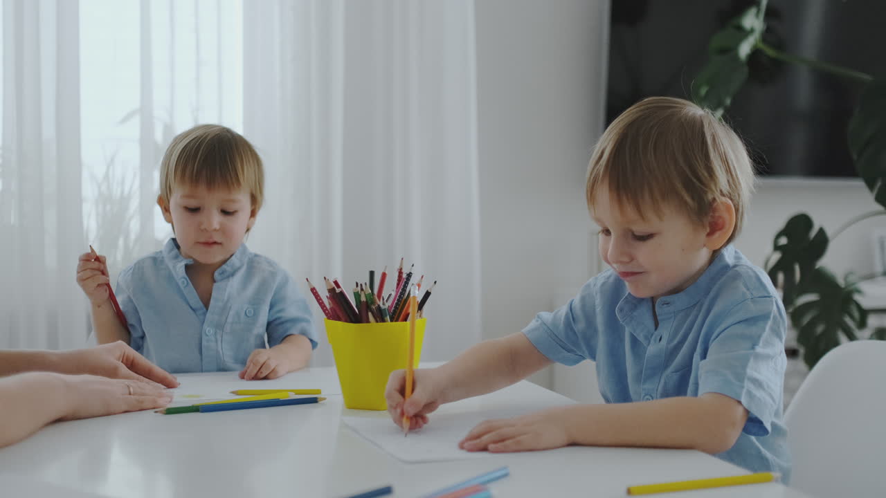 мама и ее двое сыновей сидят за кухонным столом и рисуют цветными карандашами. семья рисует на газоне летом. мальчики учатся рисовать, а мама помогает рисовать.