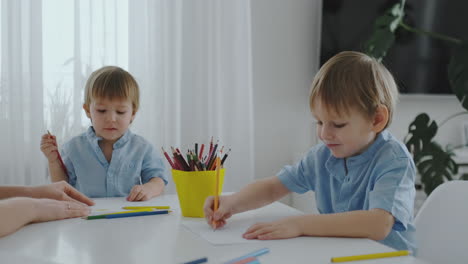 Mom-and-her-two-sons-sitting-at-the-kitchen-table-drawing-colored-pencils-family-drawing-on-the-lawn-in-the-summer.-Boys-learn-to-draw,-and-mom-helps-with-drawing