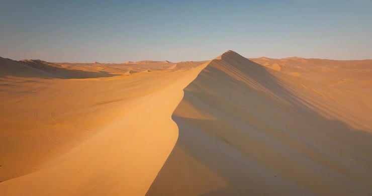 Dronebeeld over gouden zandduinen in de Huacachina-woestijn bij zonsondergang in Ica, Peru. Voorwaartse luchtopname