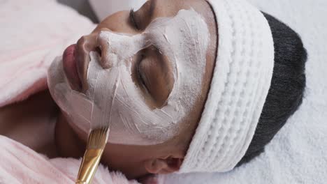 beautician applying beauty mask on face of african american plus size woman, unaltered, slow motion